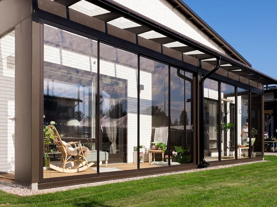 Sunroom with black-framed sliding glass walls and cozy rocking chair on a summer afternoon.