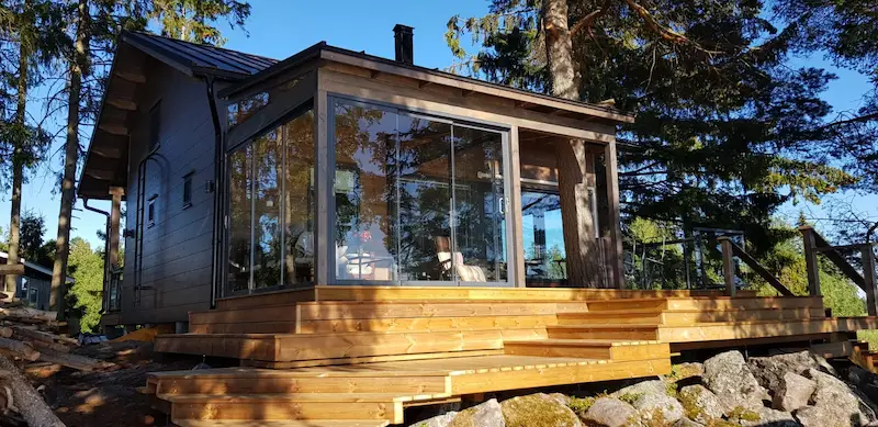 Cabin-style patio with sliding glass walls overlooking a forest and wood deck.
