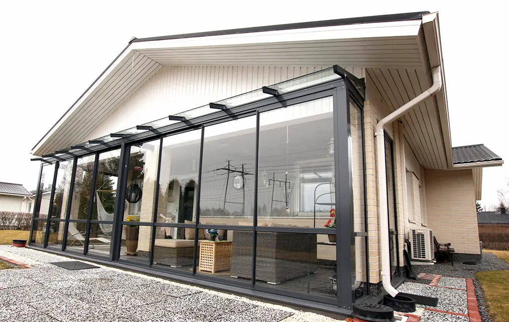Bright enclosed sunroom with sliding glass walls and modern furniture attached to a suburban home.