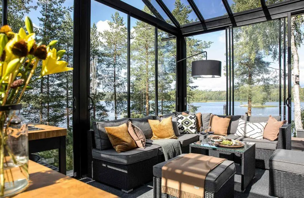 Stylish glass sunroom with sliding glass walls, black frames, and outdoor lake views.