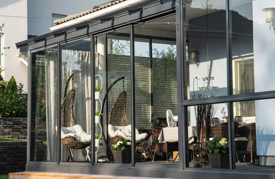 Modern sunroom with sliding glass walls and hanging wicker chairs creating a cozy indoor-outdoor retreat.