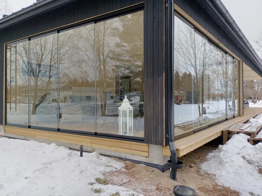 Contemporary black-framed sliding glass walls enclosing a home patio in a snowy winter setting.