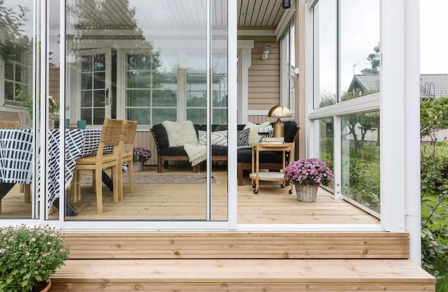 Warm wooden sunroom with white-framed sliding glass walls opening to a backyard garden.