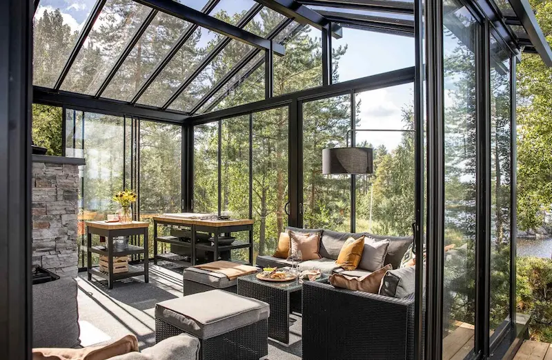 Elegant glass sunroom enclosure with black frame and panoramic reflections of trees and sky.
