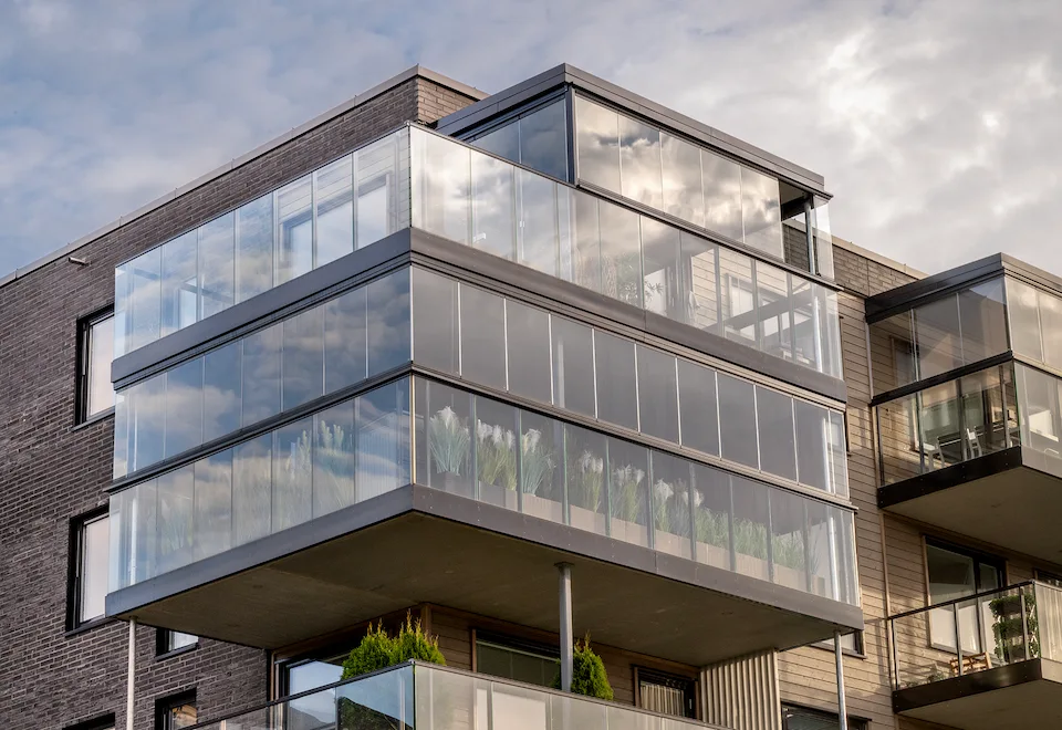 Multi-story modern apartment building showcasing enclosed balconies with glass facades and integrated railings for safety and style.
