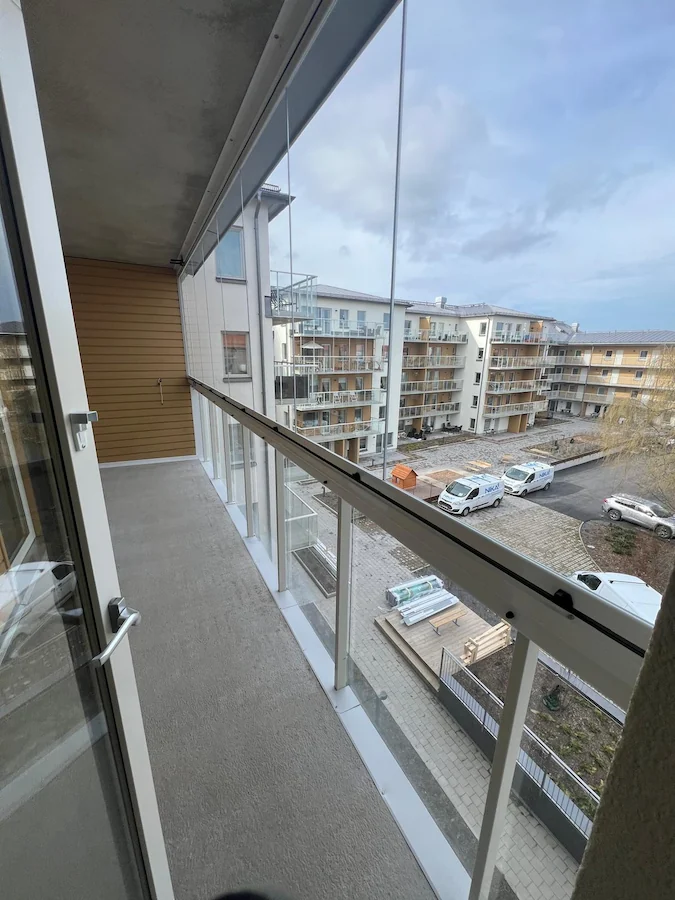 Long narrow balcony enclosed with frameless folding glass walls overlooking modern residential buildings.