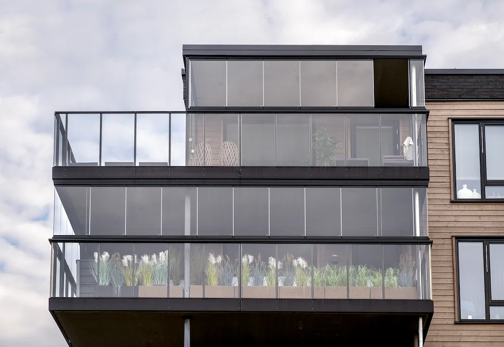 Multi-level apartment complex with balconies enclosed in frameless folding glass walls for modern urban living.