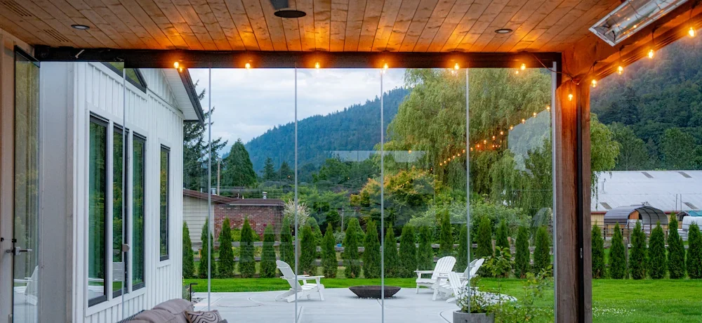 Outdoor living space with frameless folding glass walls and cozy seating, overlooking a landscaped yard.