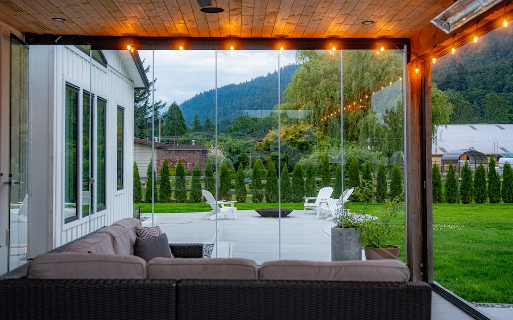 Outdoor living space with frameless folding glass walls and cozy seating, overlooking a landscaped yard.