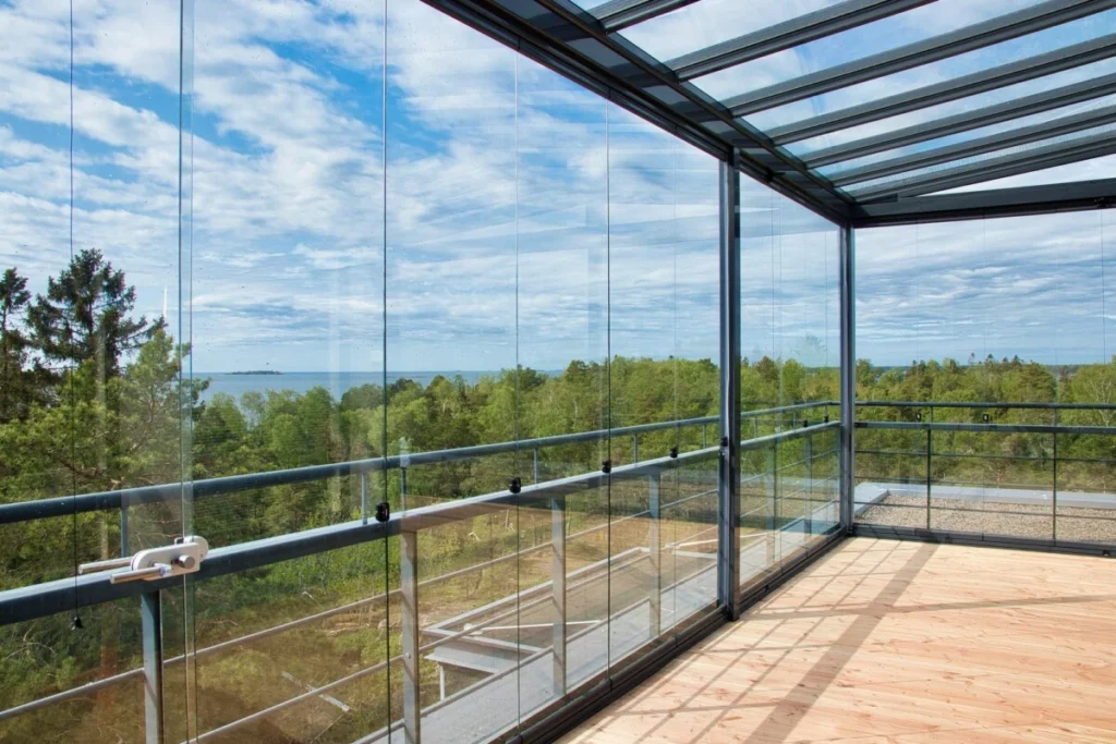 Frameless glass balcony enclosure with clear sliding panels offering panoramic views of forest and sky.