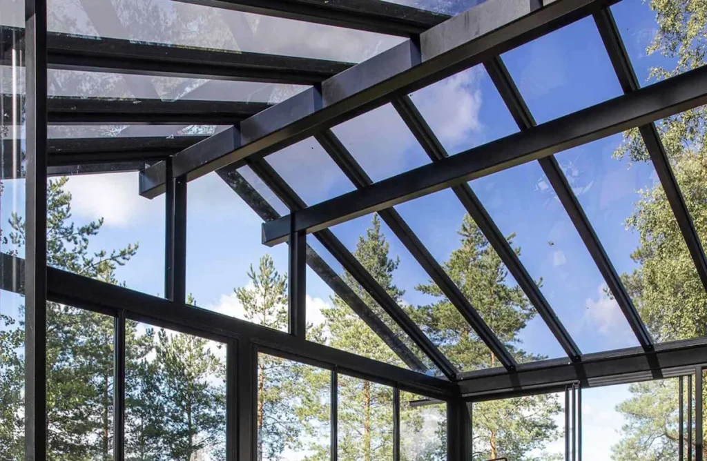 Close-up of modern glass pergola roof systems with black metal framing against a clear blue sky and tree backdrop.