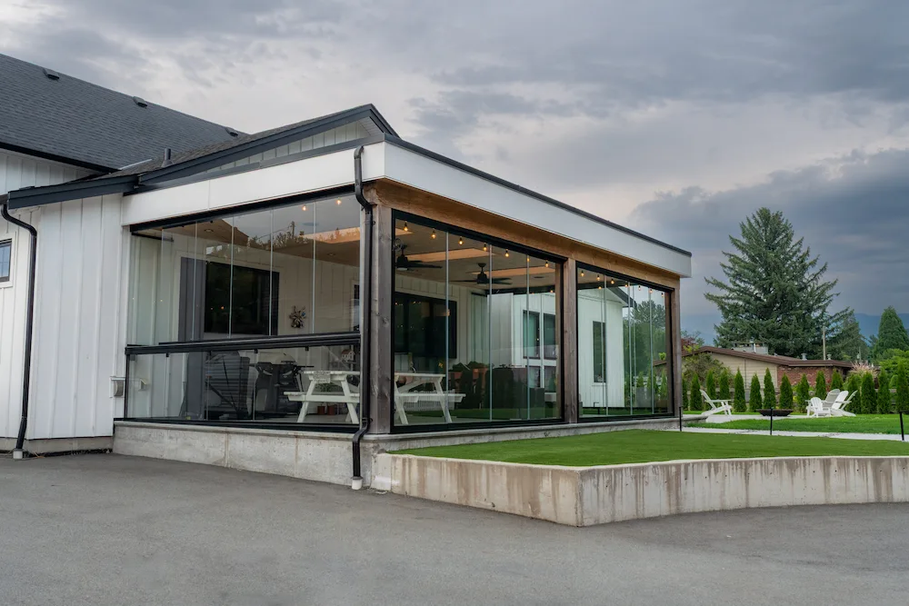 Contemporary white home with a large glass sunroom extension and integrated railings, creating an open, seamless outdoor connection.
