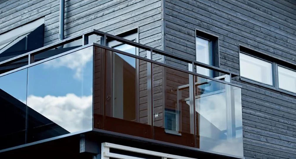 Residential balcony with clear integrated railings and glass panels, blending modern architecture with natural wood siding.