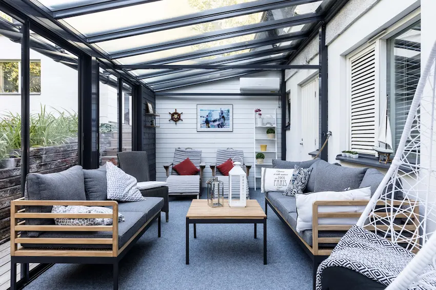 Stylish sunroom enclosure with glass walls, gray seating, and nautical-themed decor for year-round comfort.