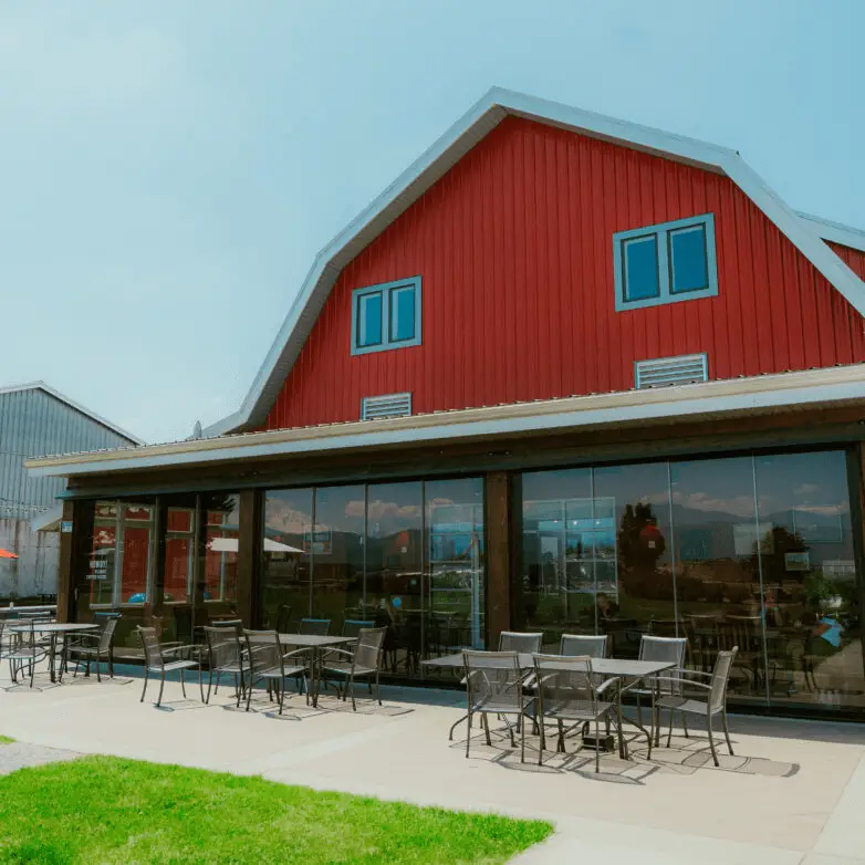 Modern red barn-style building with large glass sunroom walls and outdoor dining tables on the patio.