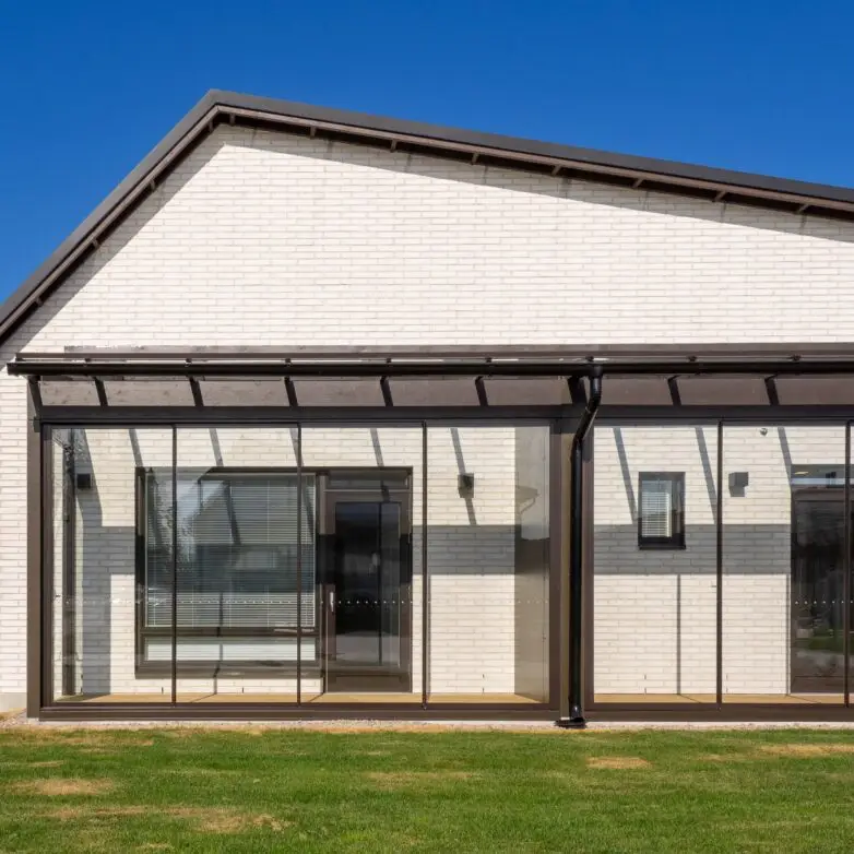 Patio enclosure with a flat glass roof and sliding glass doors, blending indoor and outdoor spaces.