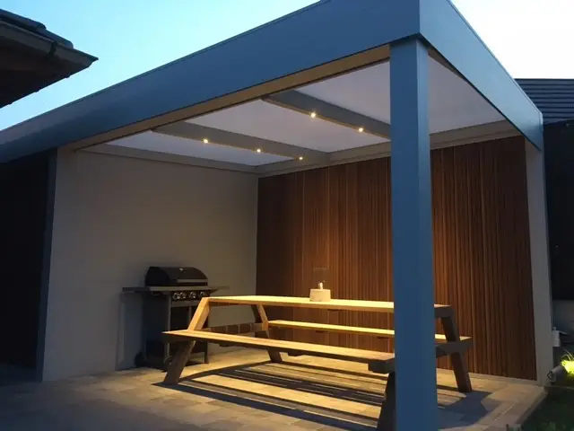 Covered outdoor dining space with a flat roof system featuring recessed lighting and modern wood paneling.