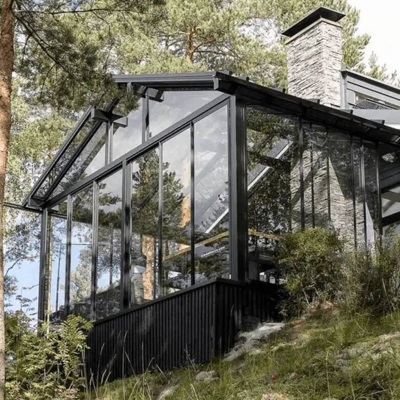 Black-framed gabled sunroom with floor-to-ceiling glass walls surrounded by forest greenery.