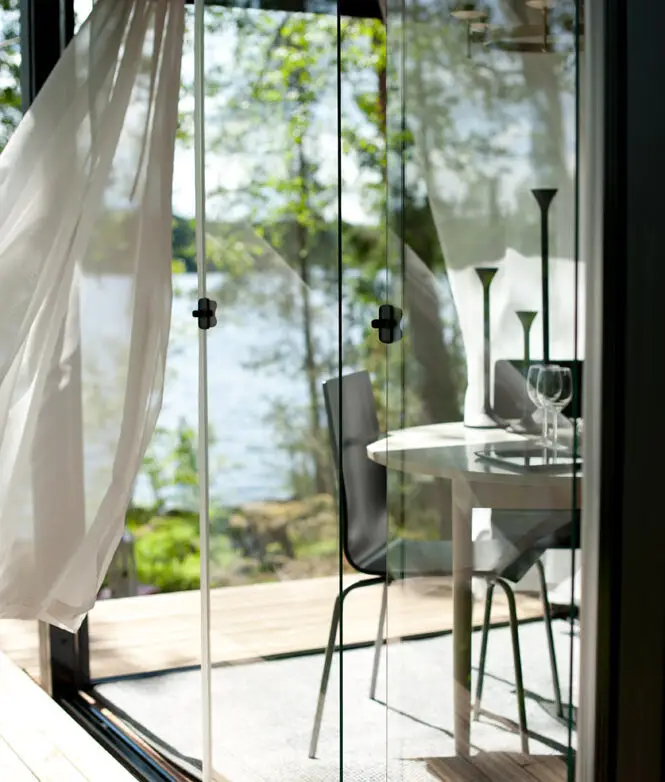 Scenic glass-enclosed dining space with floor-to-ceiling panels overlooking water views, furnished with a round table and chairs.