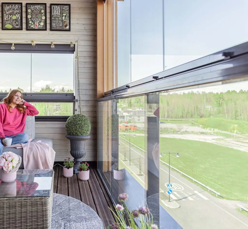 Enclosed balcony with integrated glass railings and seating, designed for year-round use in a residential building.