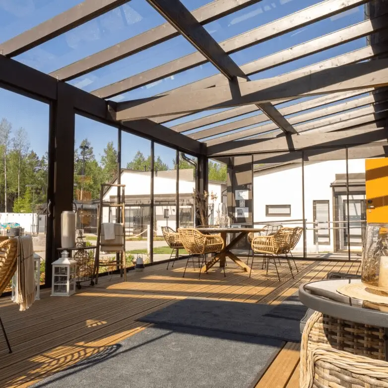 Spacious sunroom with wood furnishings beneath a transparent glass roof and framed walls, maximizing natural light.