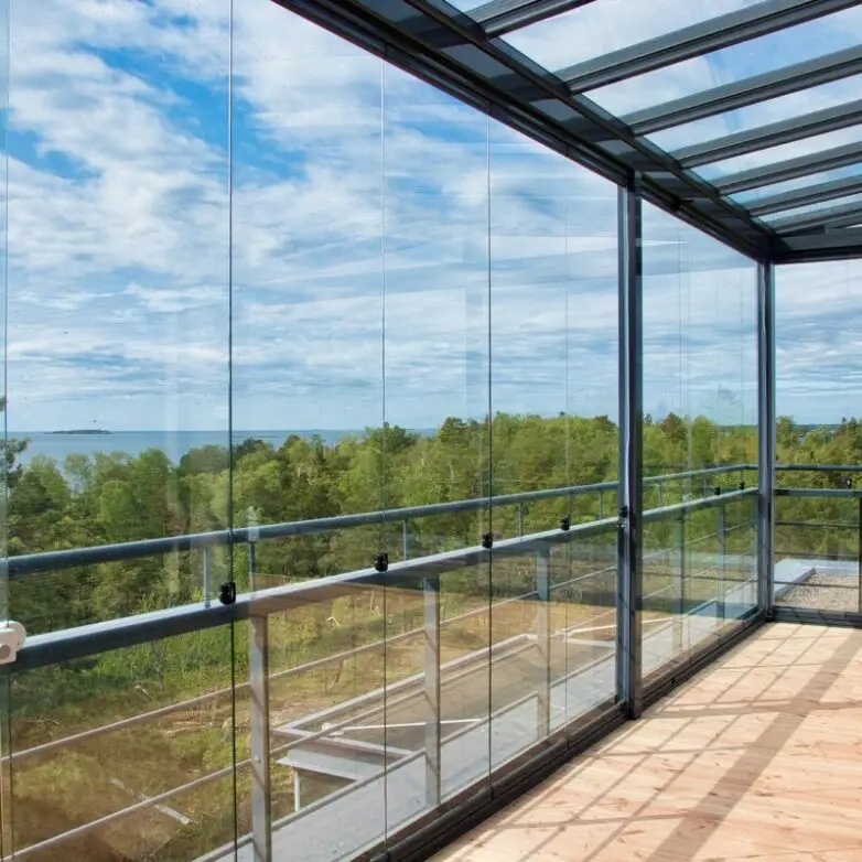 Spacious balcony with glass wall system and roof enclosure, providing panoramic ocean and forest views under clear skies.