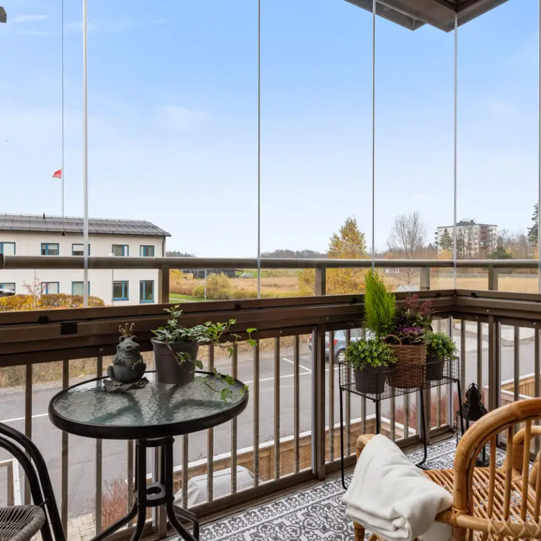 Cozy balcony with integrated glass railings, outdoor chairs, and potted plants overlooking a residential neighborhood.