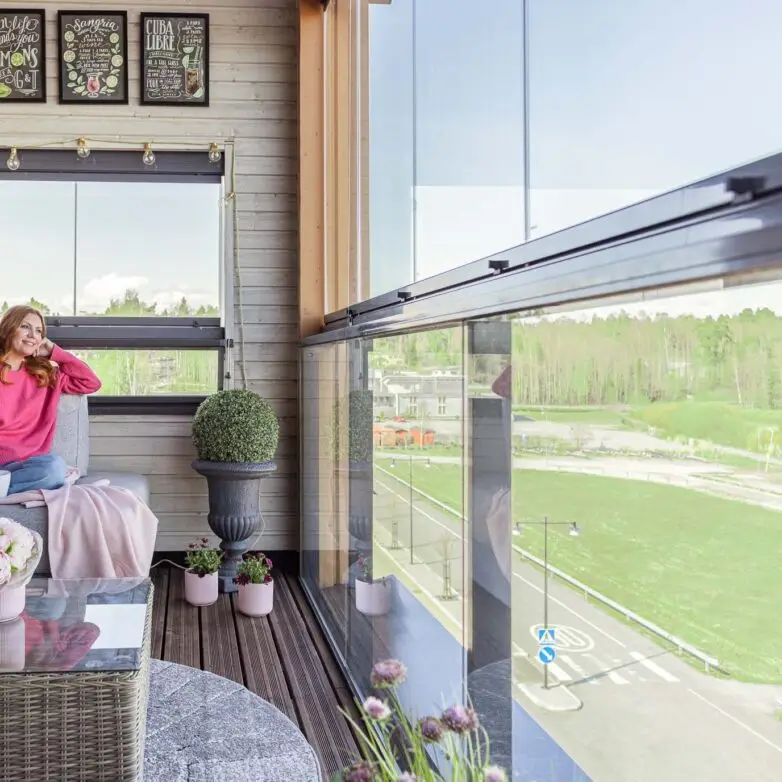 Enclosed balcony with integrated glass railings and seating, designed for year-round use in a residential building.
