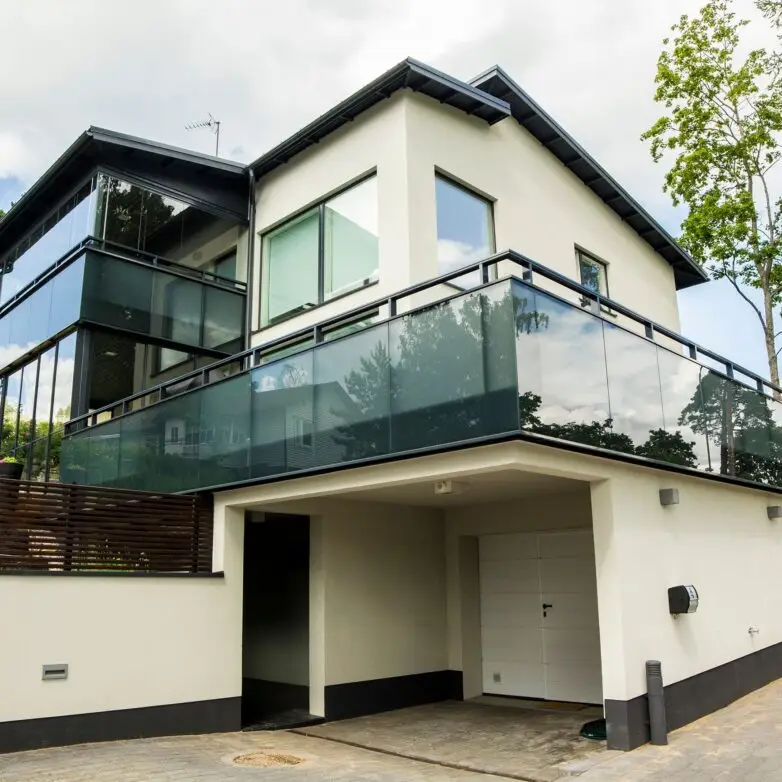 Modern home exterior with second-floor patio enclosure and integrated glass railings in dark frames.