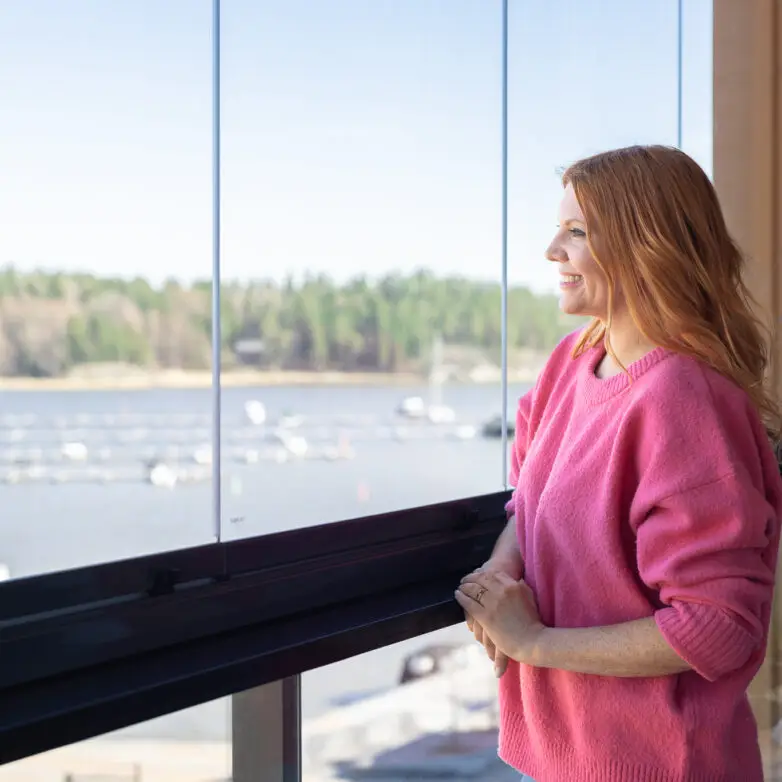 Woman enjoying waterfront views from a balcony with integrated glass railings on a sunny day.