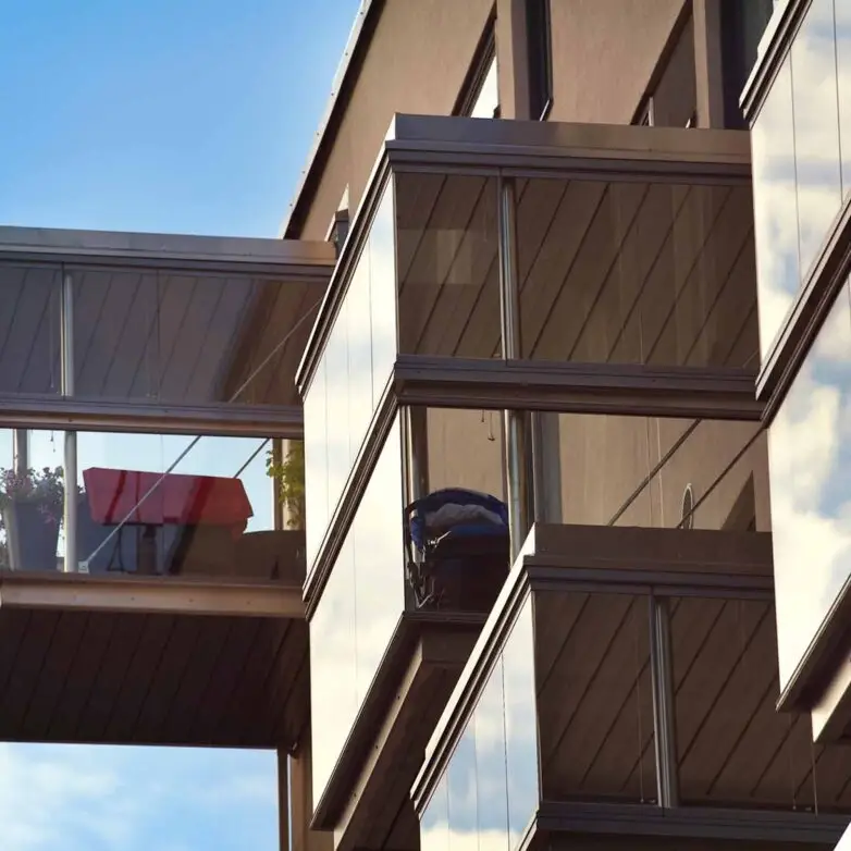 Modern residential building with fully enclosed glass balconies, offering weather-protected outdoor living areas.
