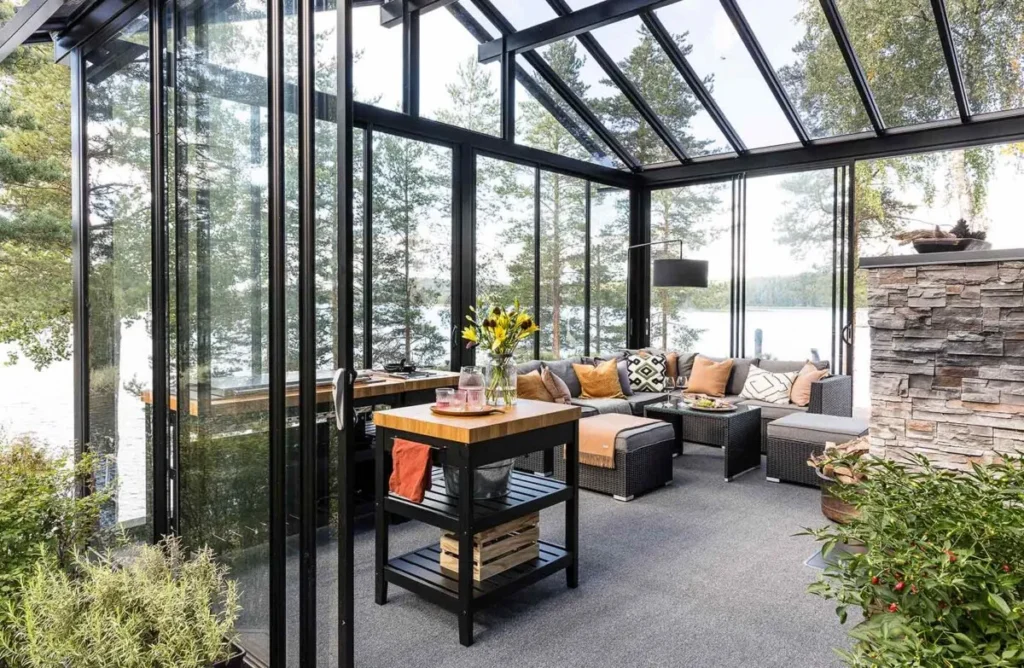 Stylish glass sunroom with floor-to-ceiling windows, wicker sectional sofa, and garden views creating a modern outdoor living space.