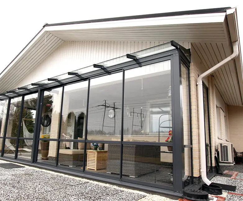 Modern home with full glass wall patio enclosure addition, featuring black framing and indoor lounge furniture for year-round use.