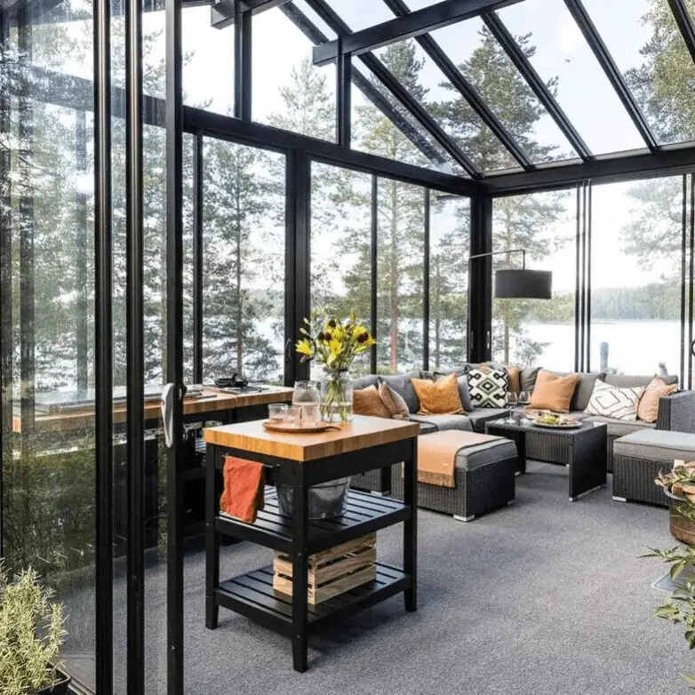 Contemporary sunroom with glass walls and pitched roof, featuring wicker sectional seating and lake views.