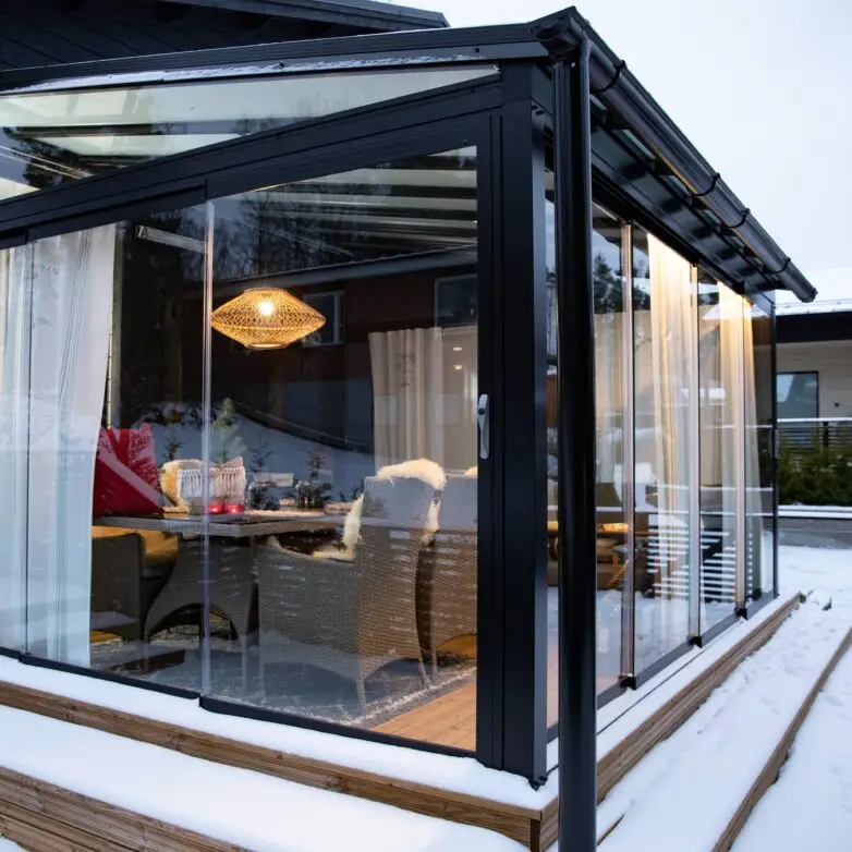 Restaurant patio enclosure with floor-to-ceiling glass walls creating an indoor-outdoor dining space with metal tables and chairs.