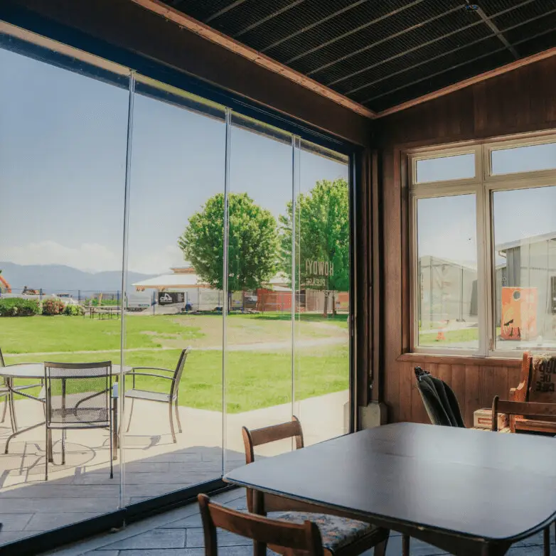 Indoor dining area with wide glass sliding walls opening to a green lawn and patio seating outside.
