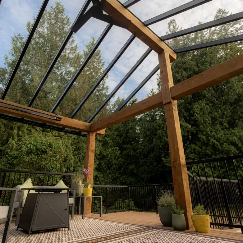 Outdoor patio enclosure with glass roof supported by wood beams, surrounded by trees for a natural setting.